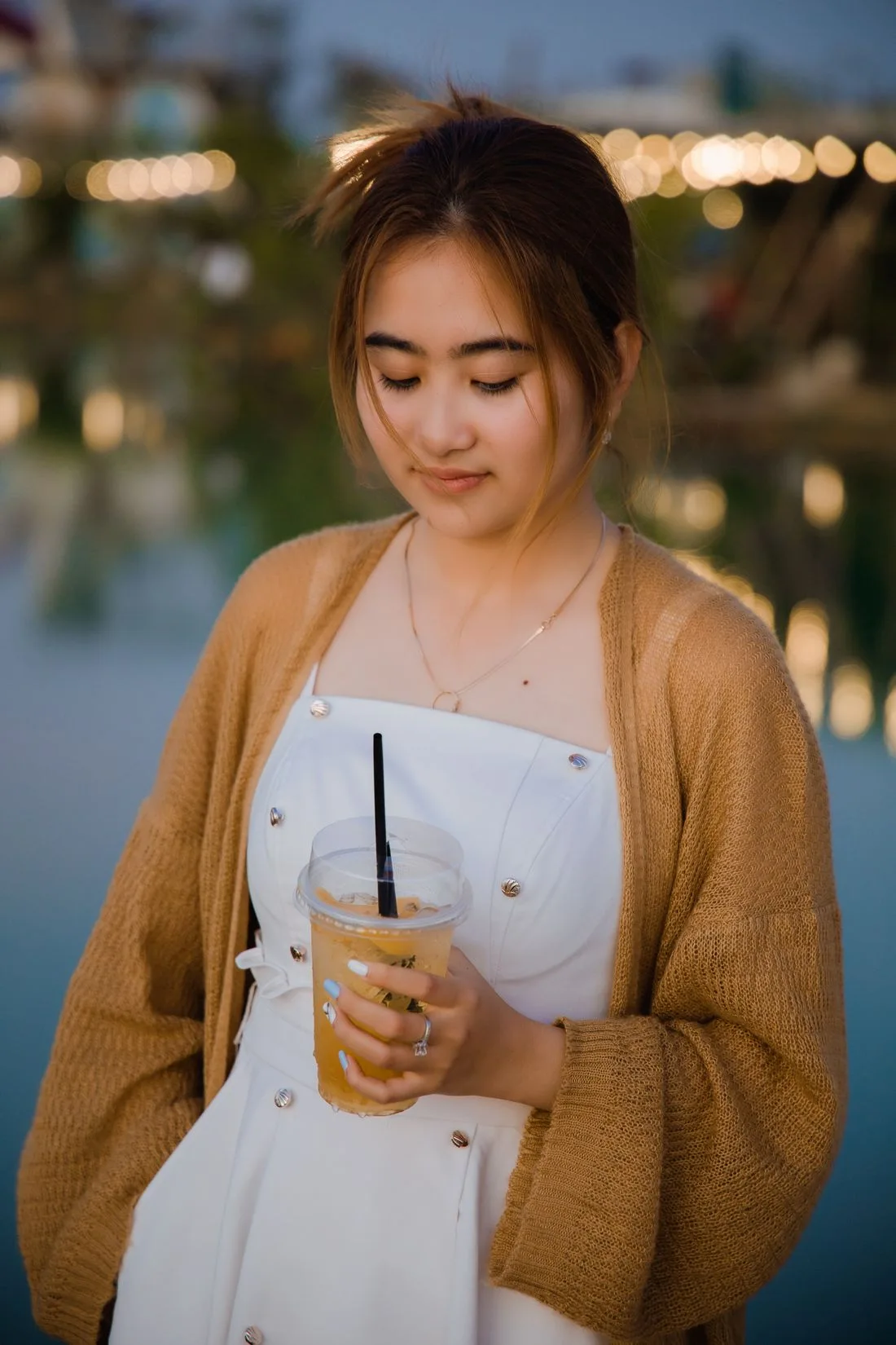 Woman wearing a cardigan over a white dress and holding a drink