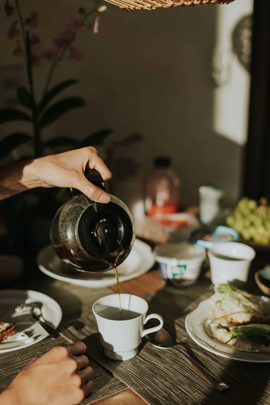 Coffee being poured at a breakfast table with cups and food.