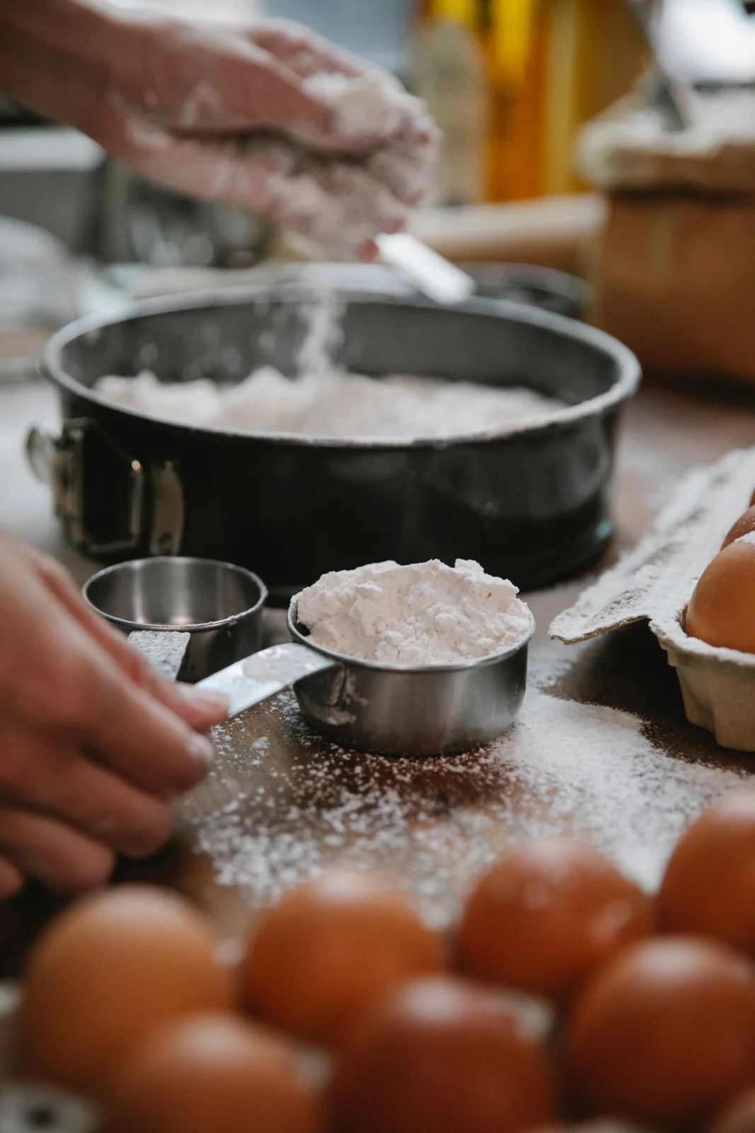 Flour, measuring cups and eggs beside a round springform baking pan
