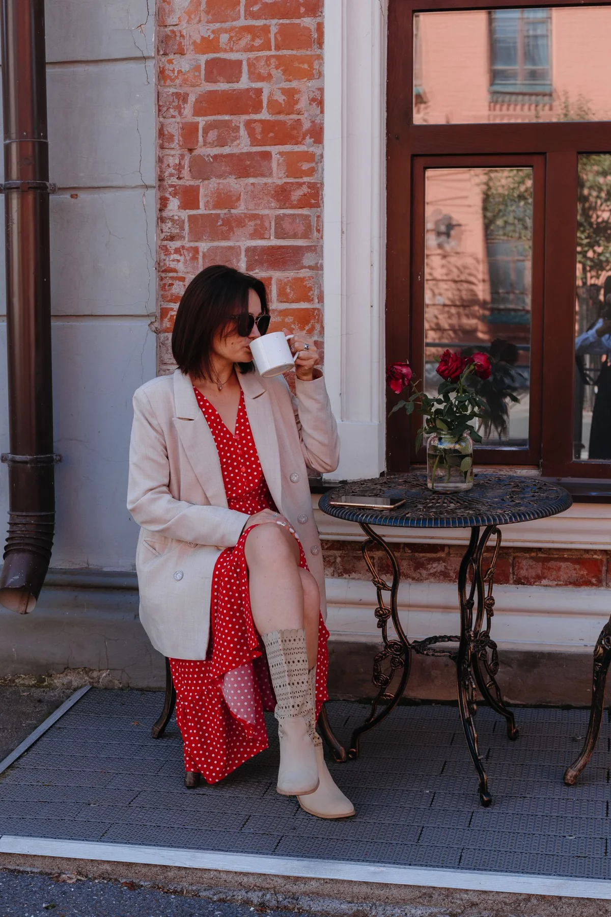 Woman in a patterned dress drinking coffee at a sidewalk cafe.