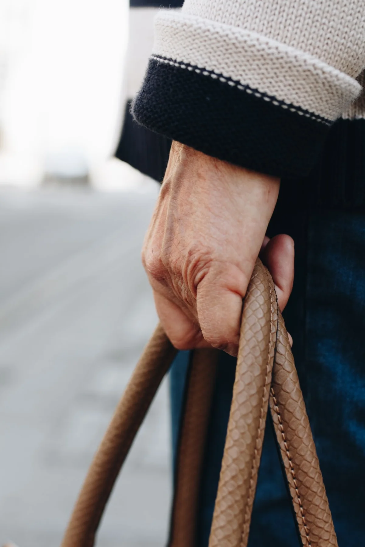 Close-up of a person in a dark sleeve carrying a textured brown handbag outdoors.