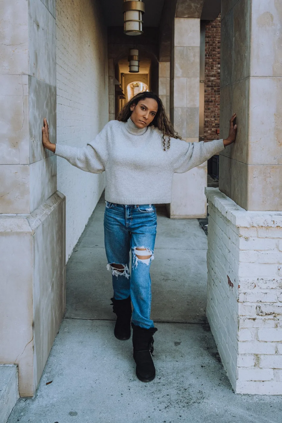 Woman wearing jeans and a white sweater in a stone alley