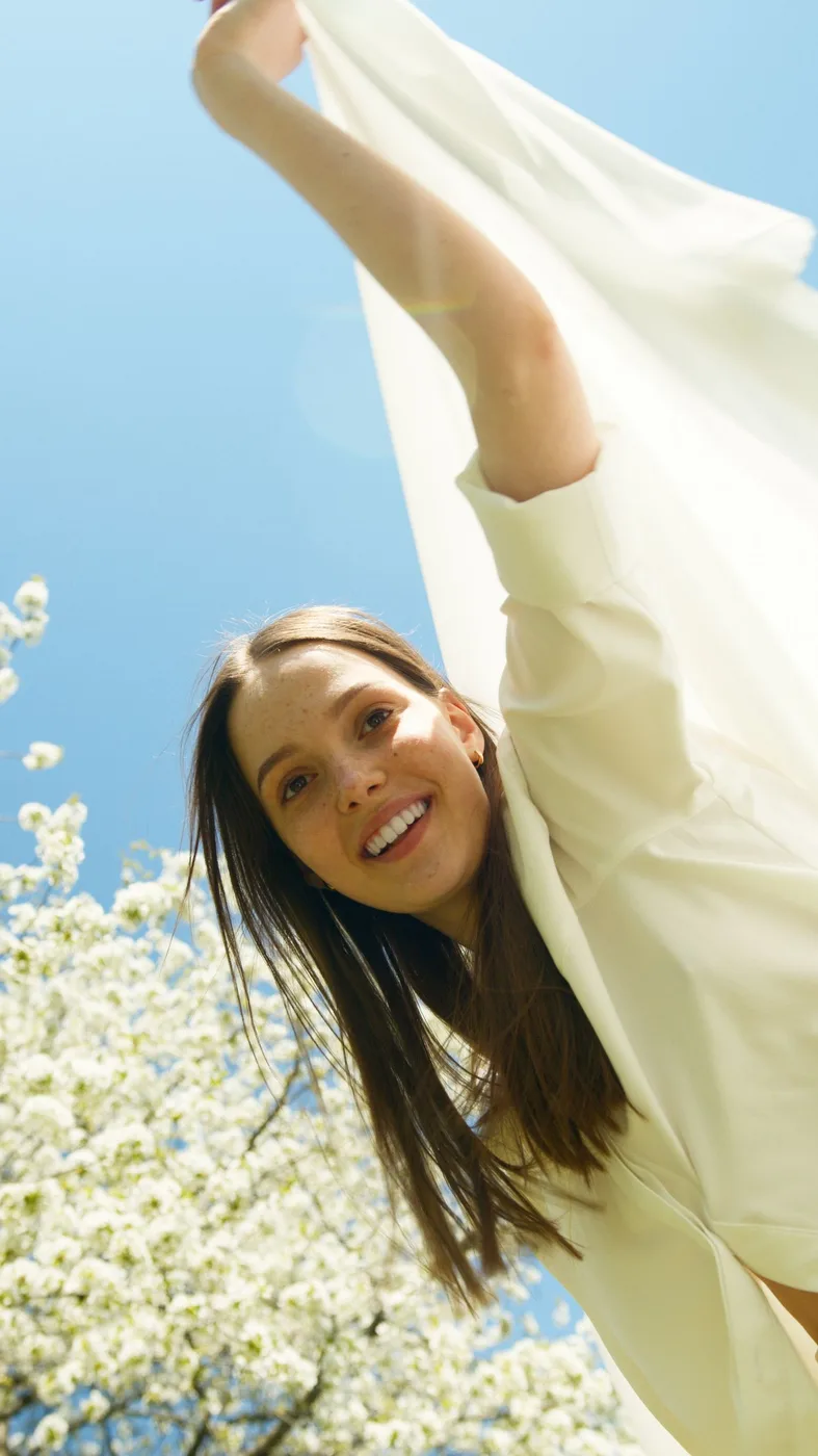 Woman in a light long-sleeved top outdoors beside flowering trees