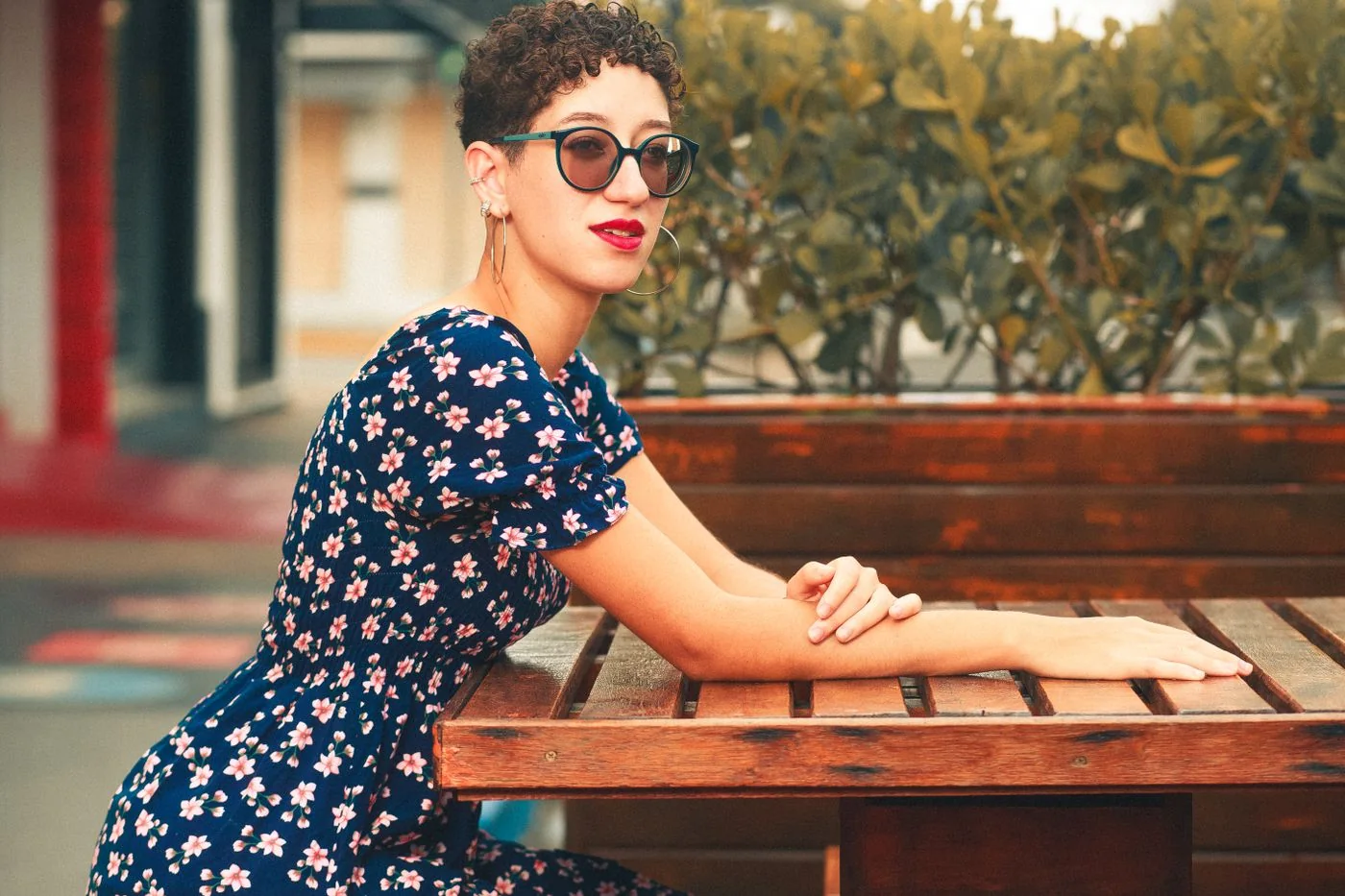 Woman in a floral dress and sunglasses seated at an outdoor cafe table.