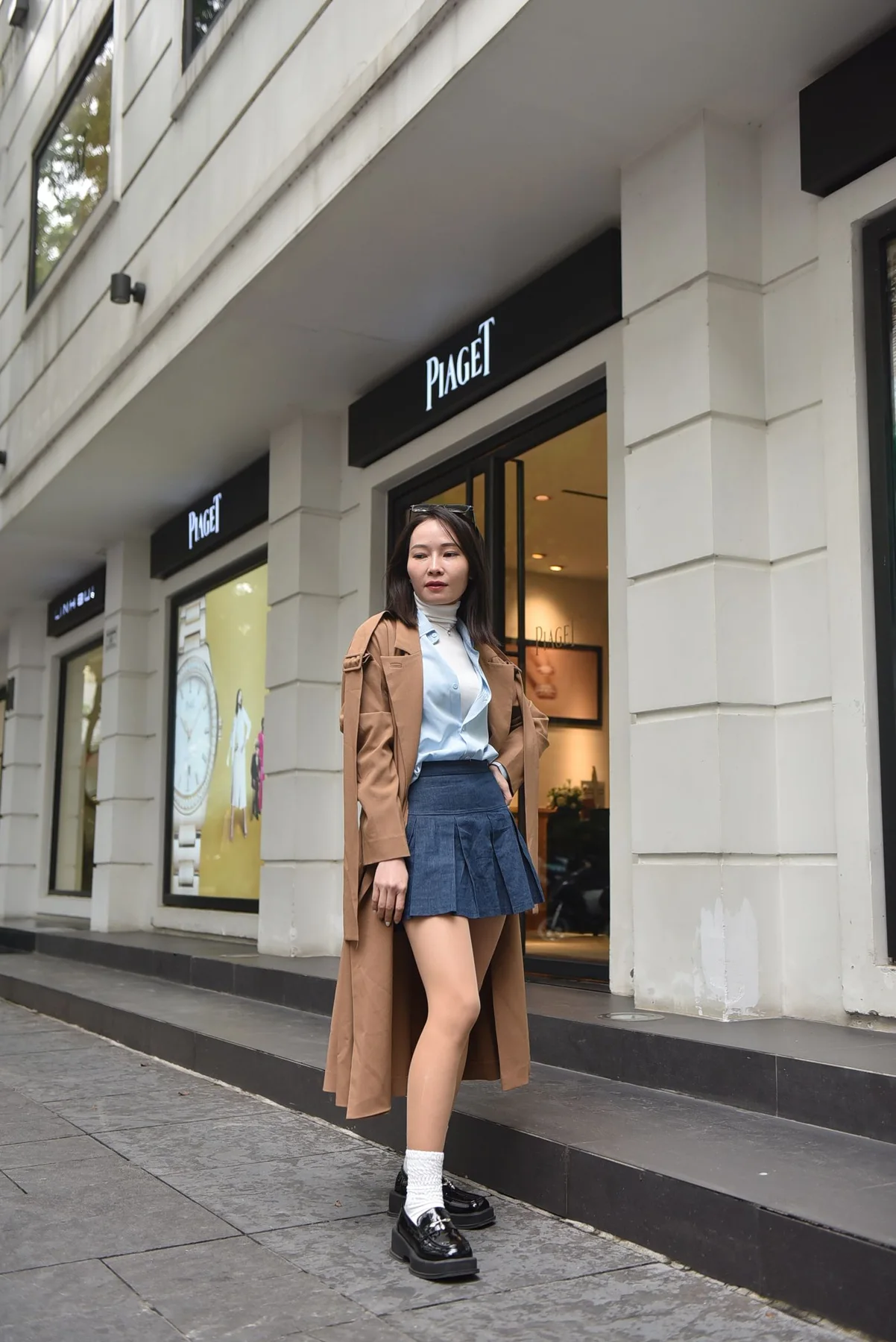 A woman wearing a brown coat, pale blouse and dark shorts on a street