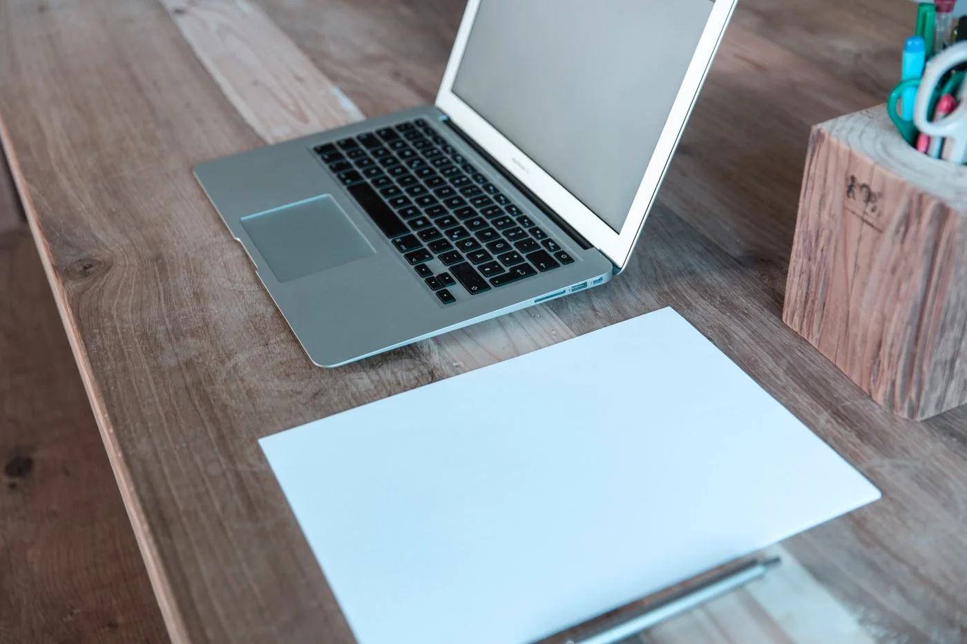A laptop and blank paper on a wooden desk