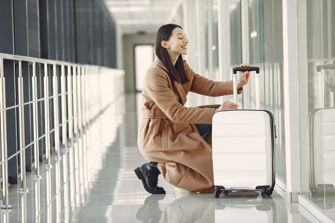 Woman in a coat seated beside her suitcase in a travel terminal