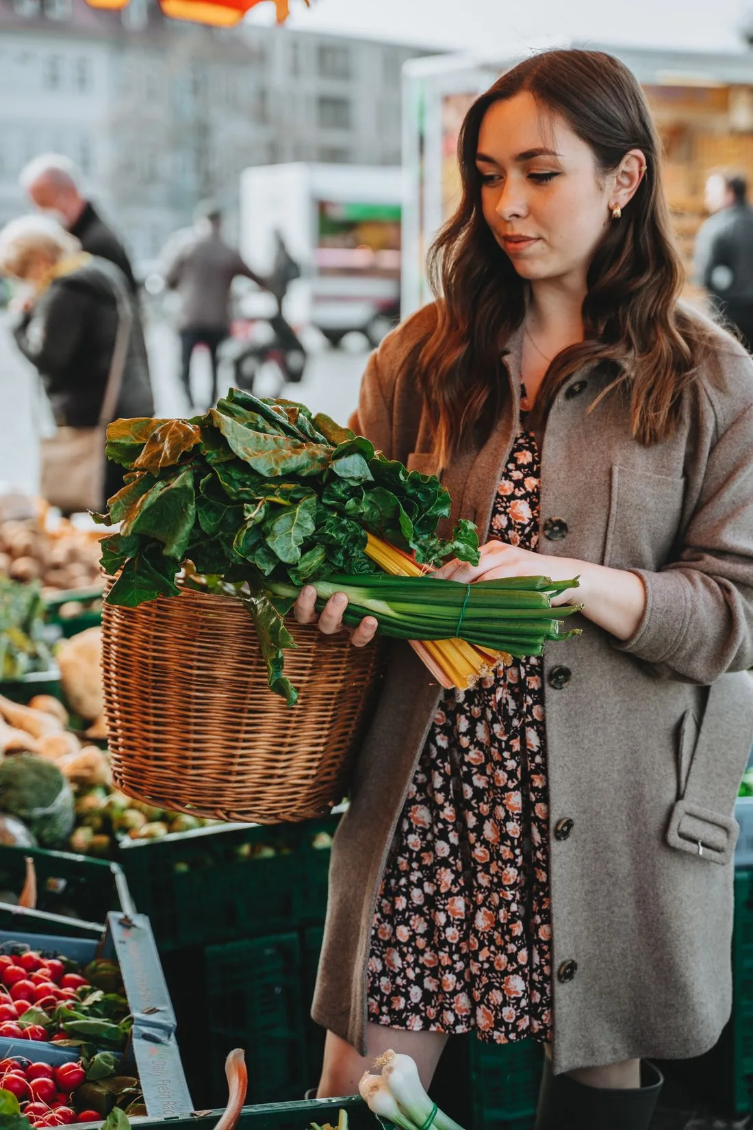 Woman with a woven basket selecting greens at an outdoor market
