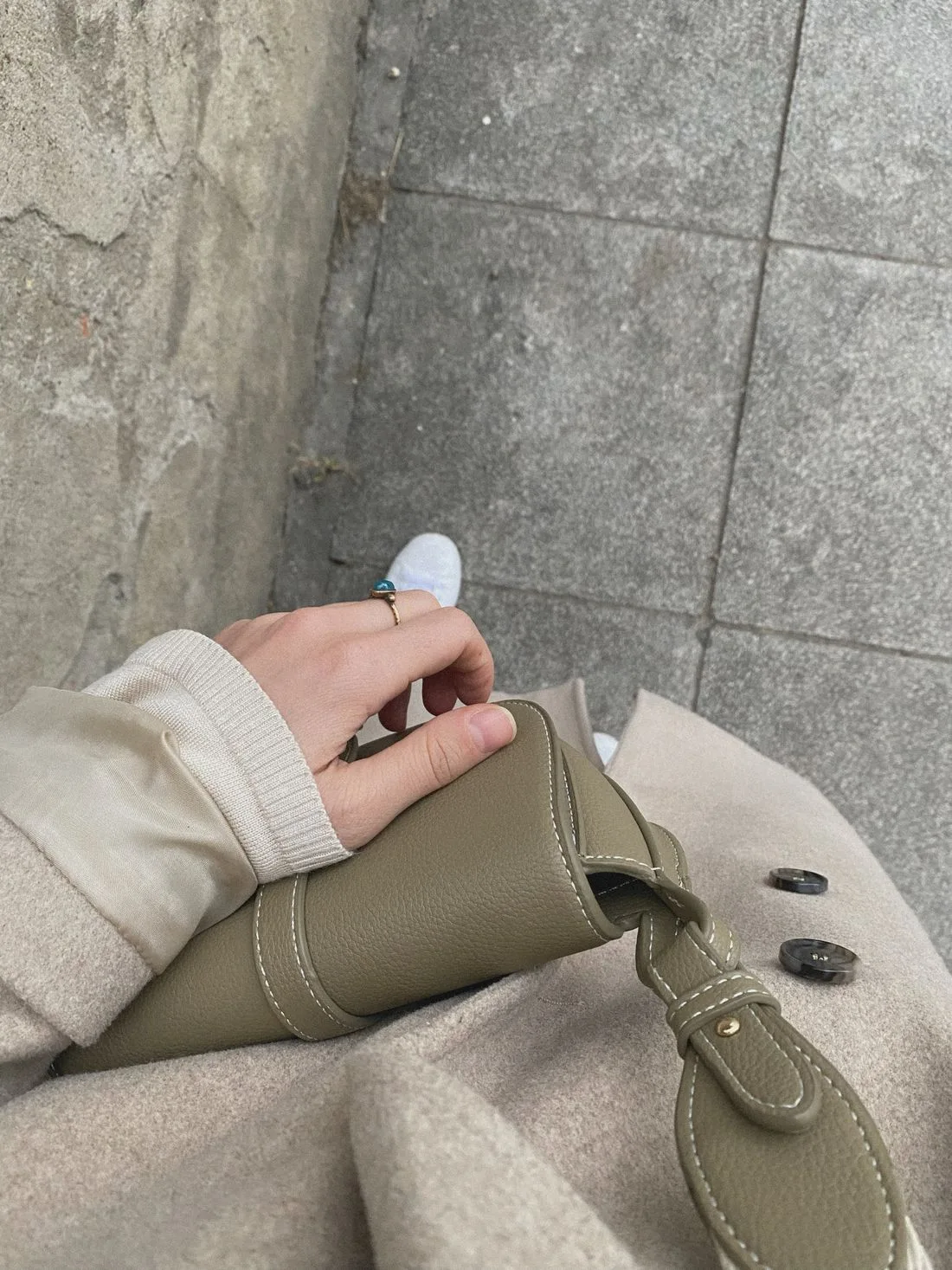 A hand resting on a green handbag beside a beige coat