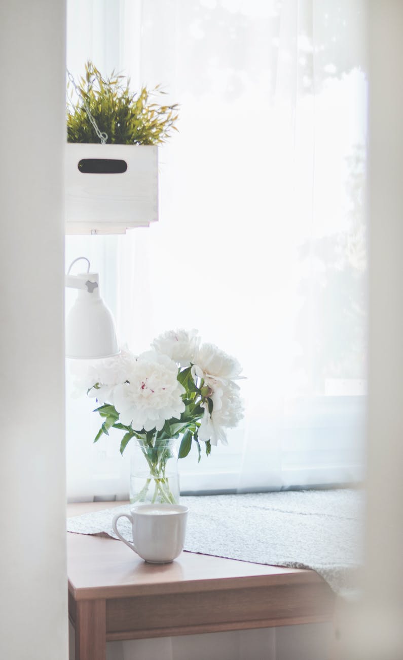 white peonies in clear glass vase centerpiece near a white ceramic mug closeup photography