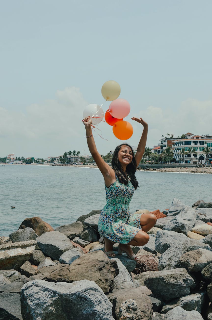 woman sitting while holding balloons near body of water