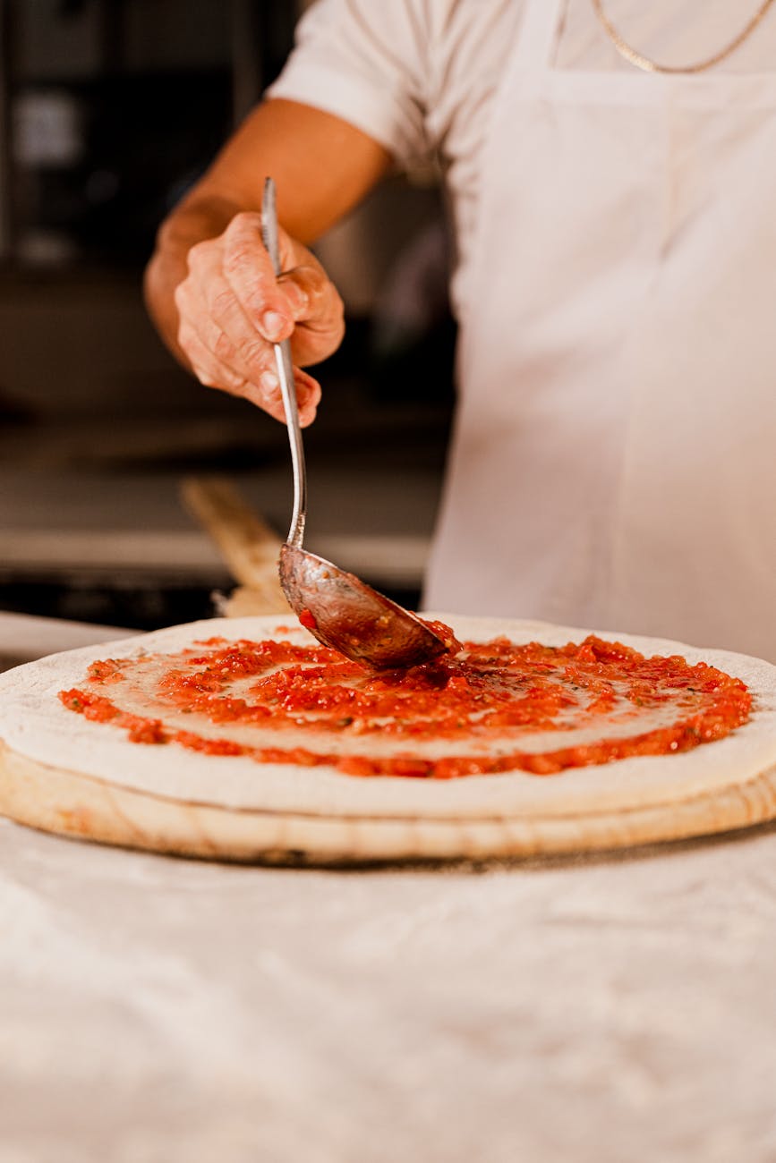man adding sauce to pizza