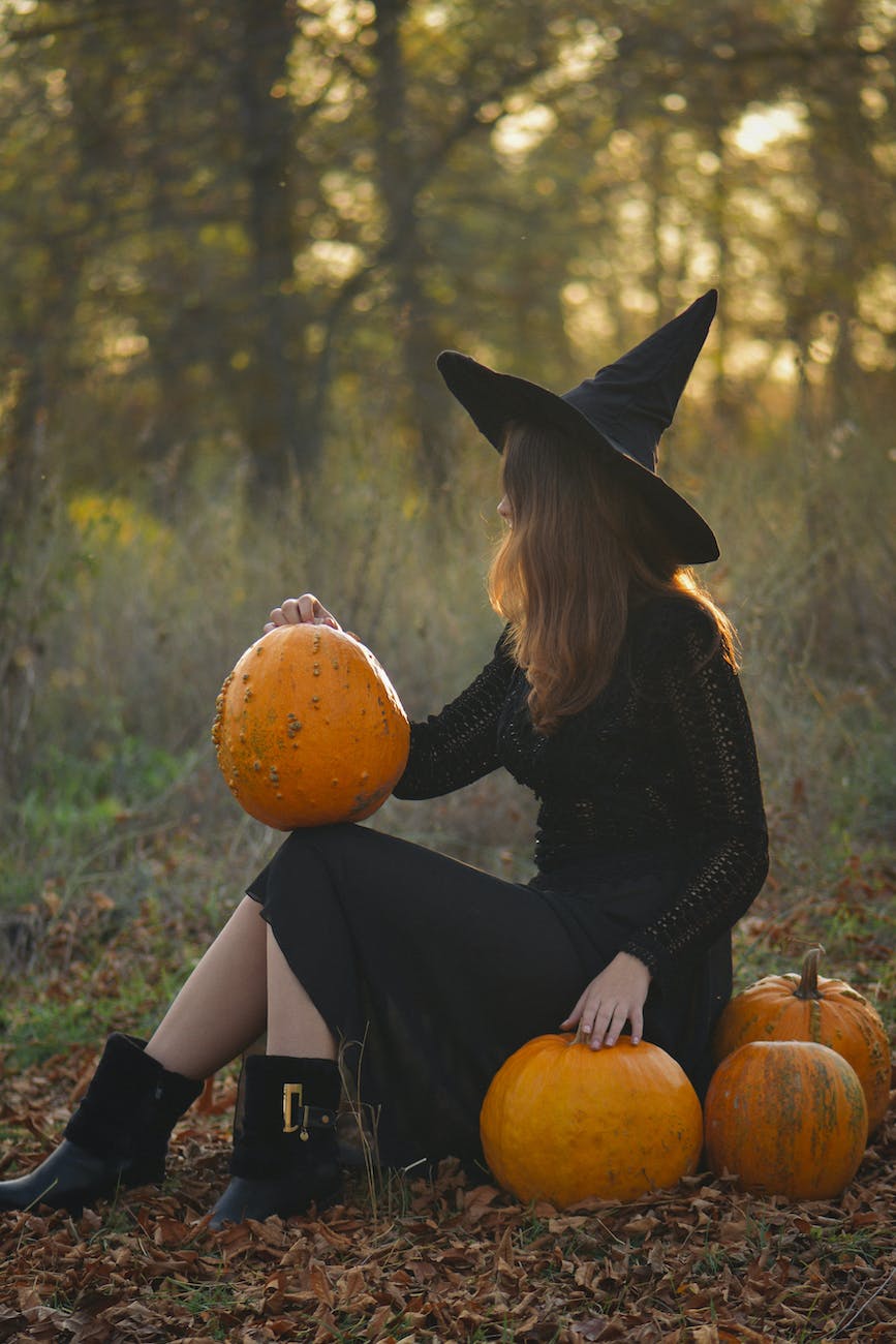 woman in a witch costume sitting among pumpkins