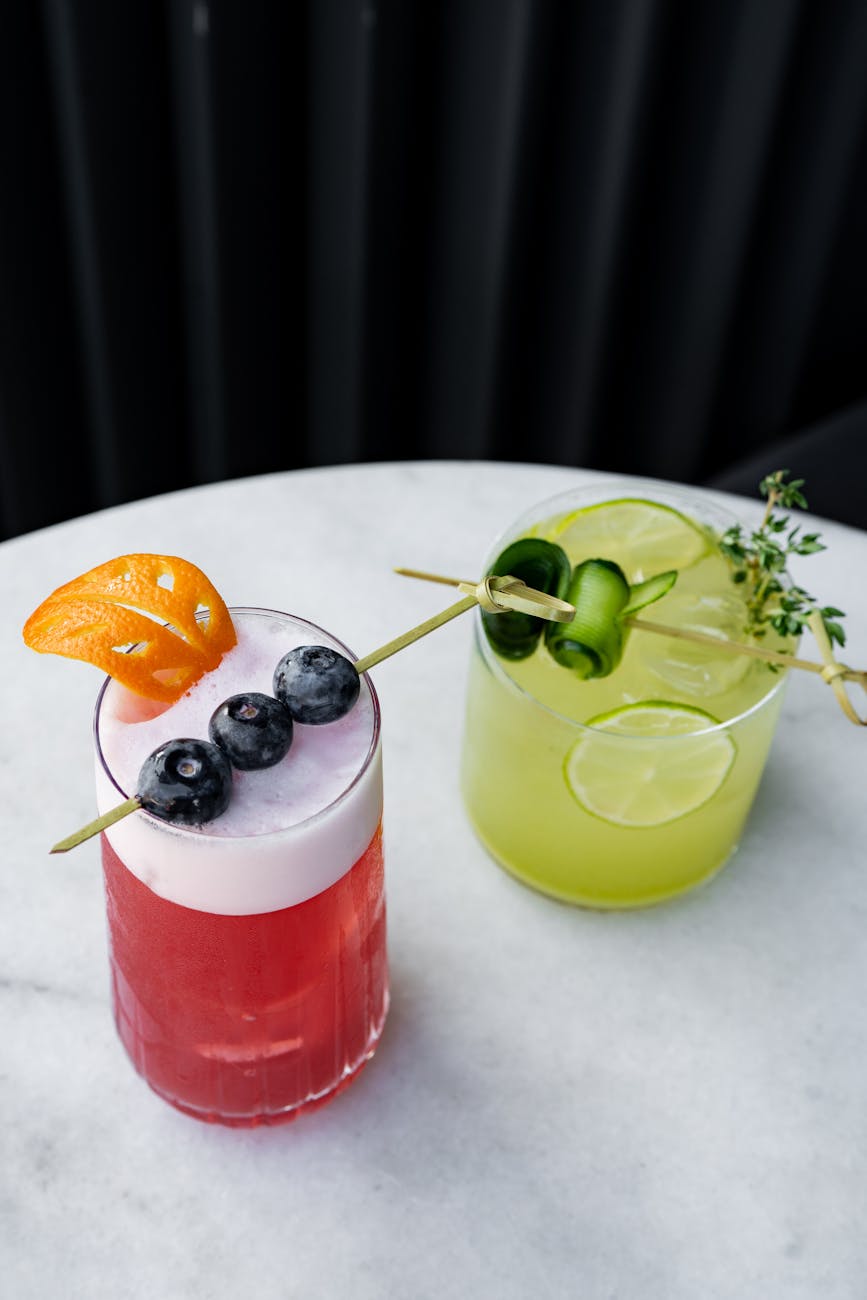 two cocktails with fruit and garnish on a marble table