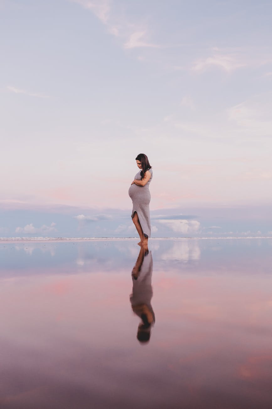 standing pregnant woman reflecting on body of water