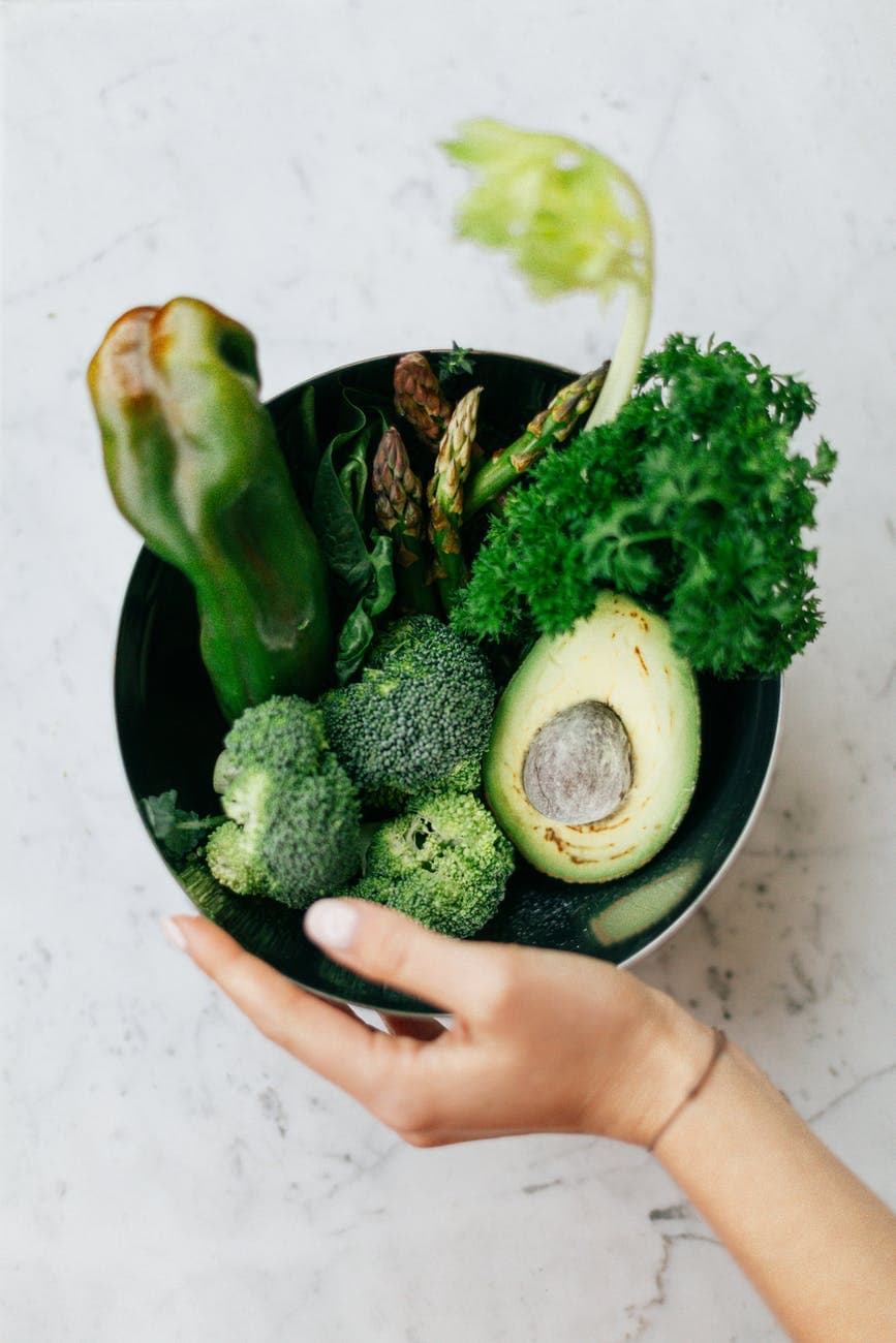 photo of female hand holding a bowl of green vegetables