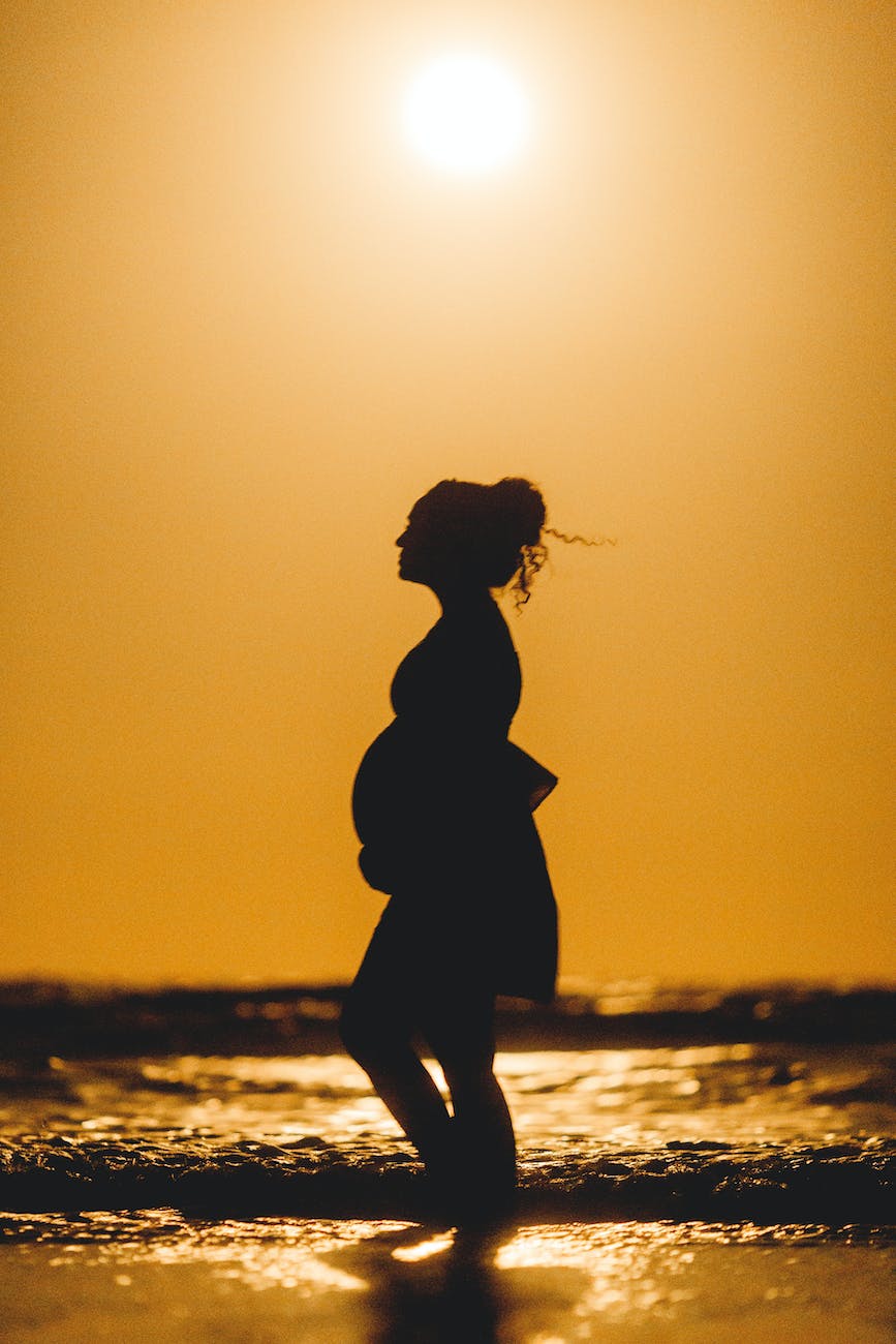 silhouette of a pregnant woman standing on beach during sunset
