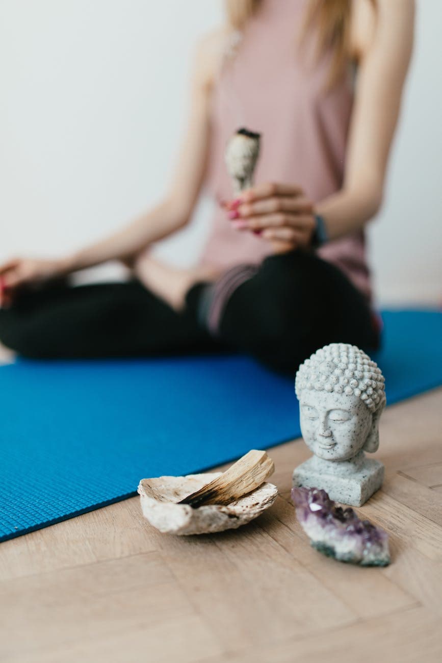 anonymous young woman sitting on floor in ardha padmasana position near esoteric objects used for meditation
