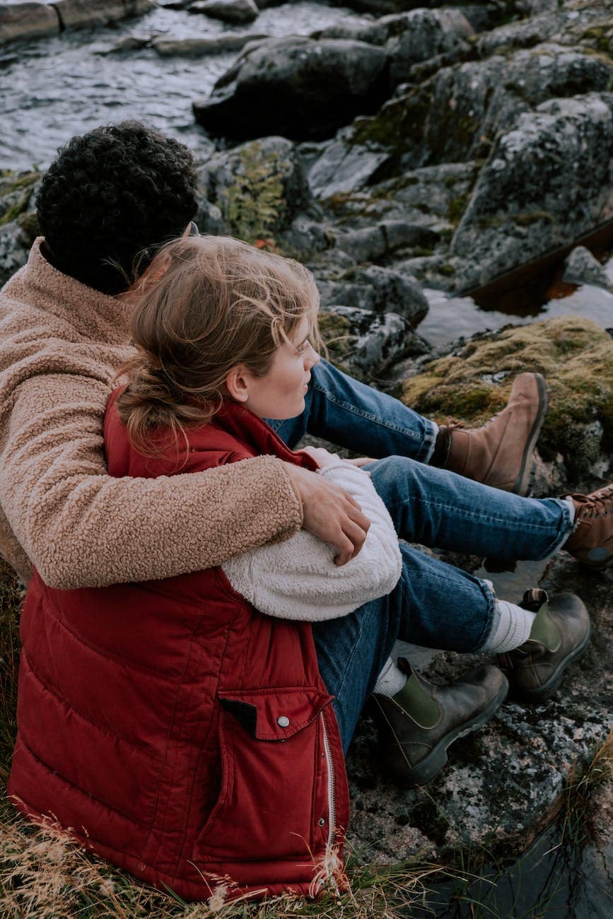 couple sitting on rock near body of water