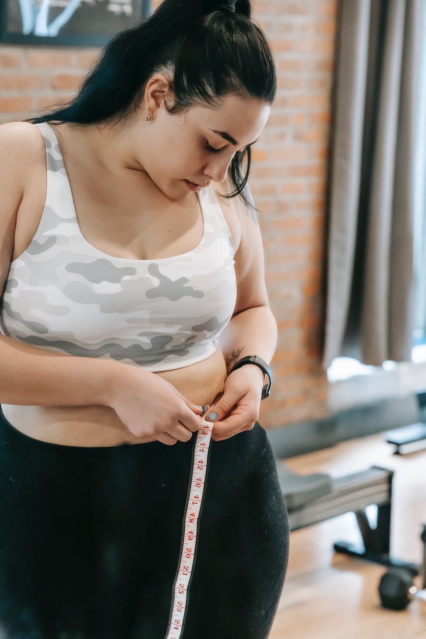 woman measuring waist with tape in gym