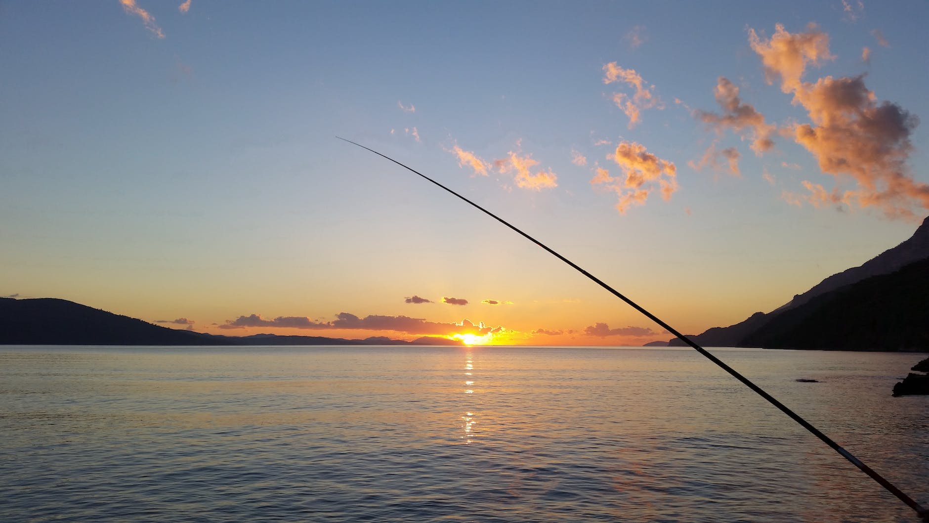fishing rod near body of water during sunset