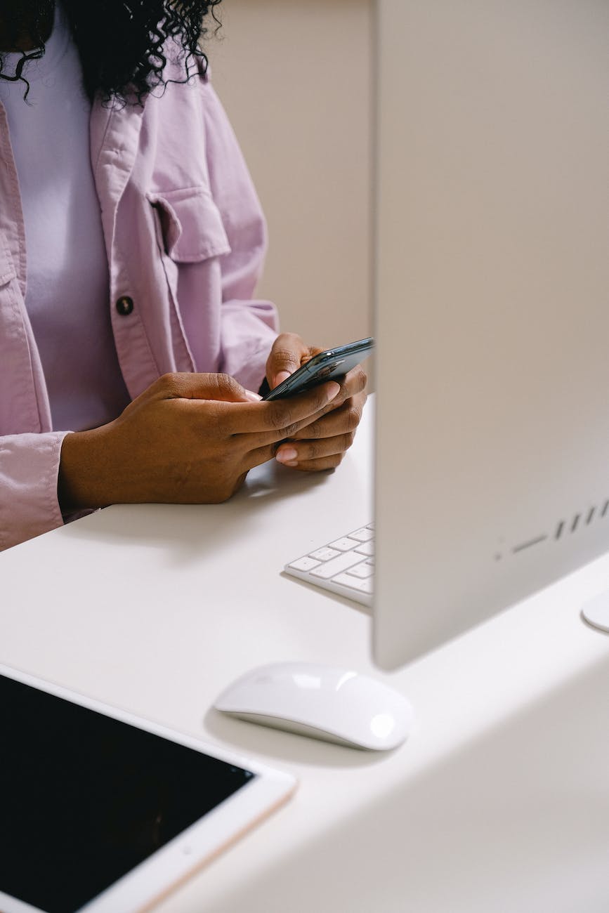 black woman texting message on smartphone at table with computer