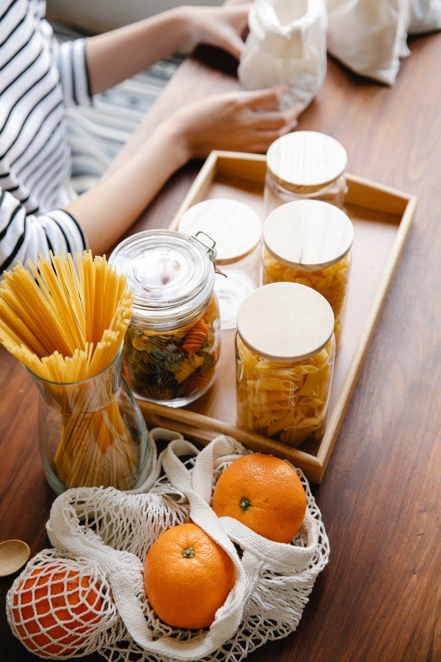 crop person holding white bag on table near fruits and pasta