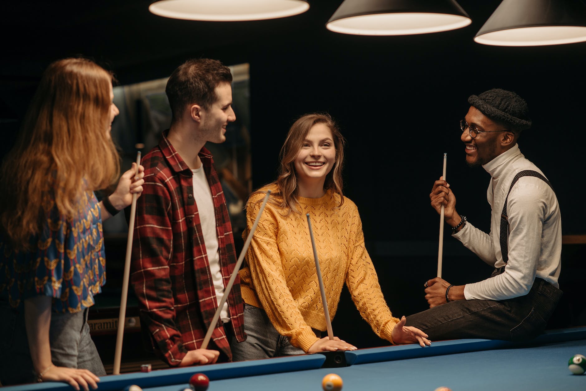 smiling women and men holding cue sticks at a pool table