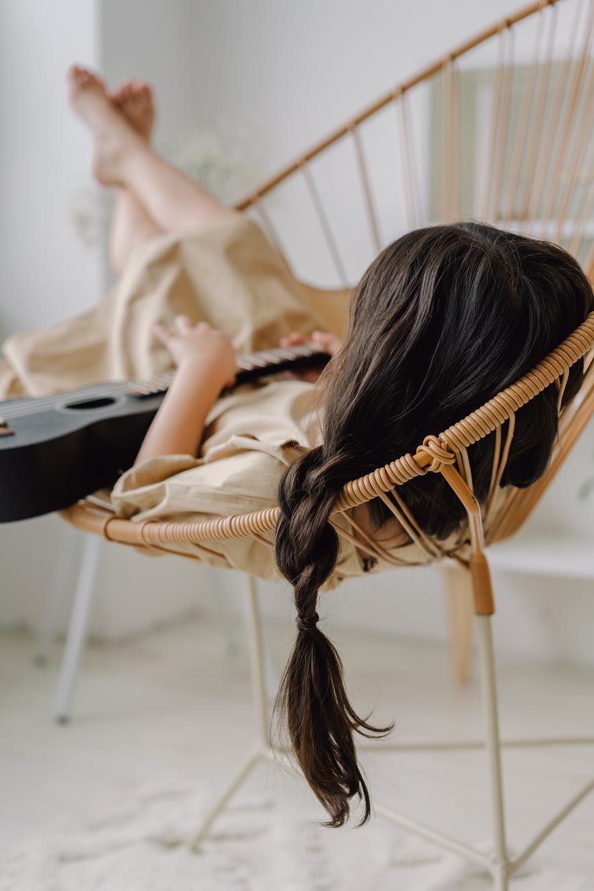 a kid lying down on a wooden chair while holding an ukelele