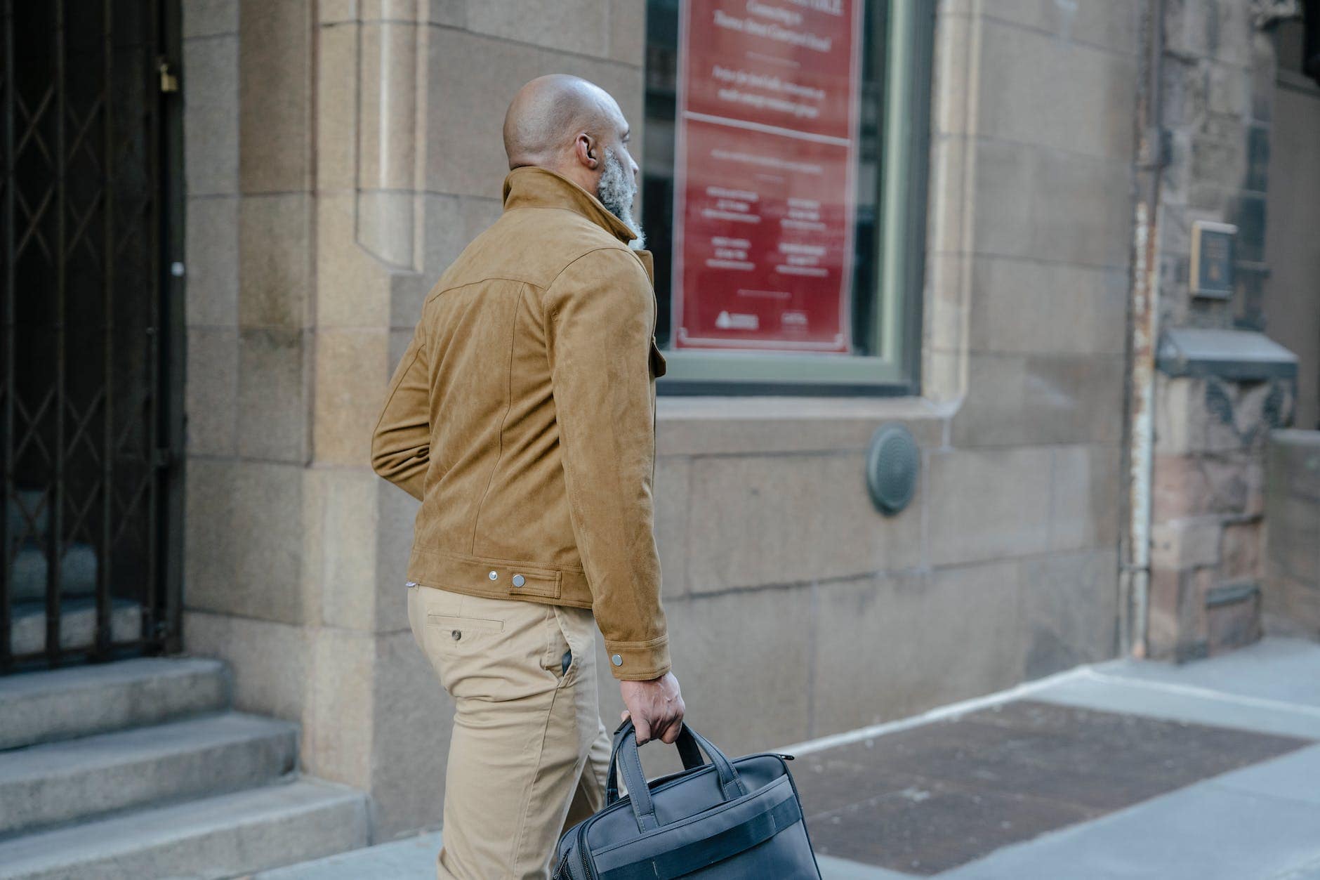 man in beige jacket walking with a briefcase on street