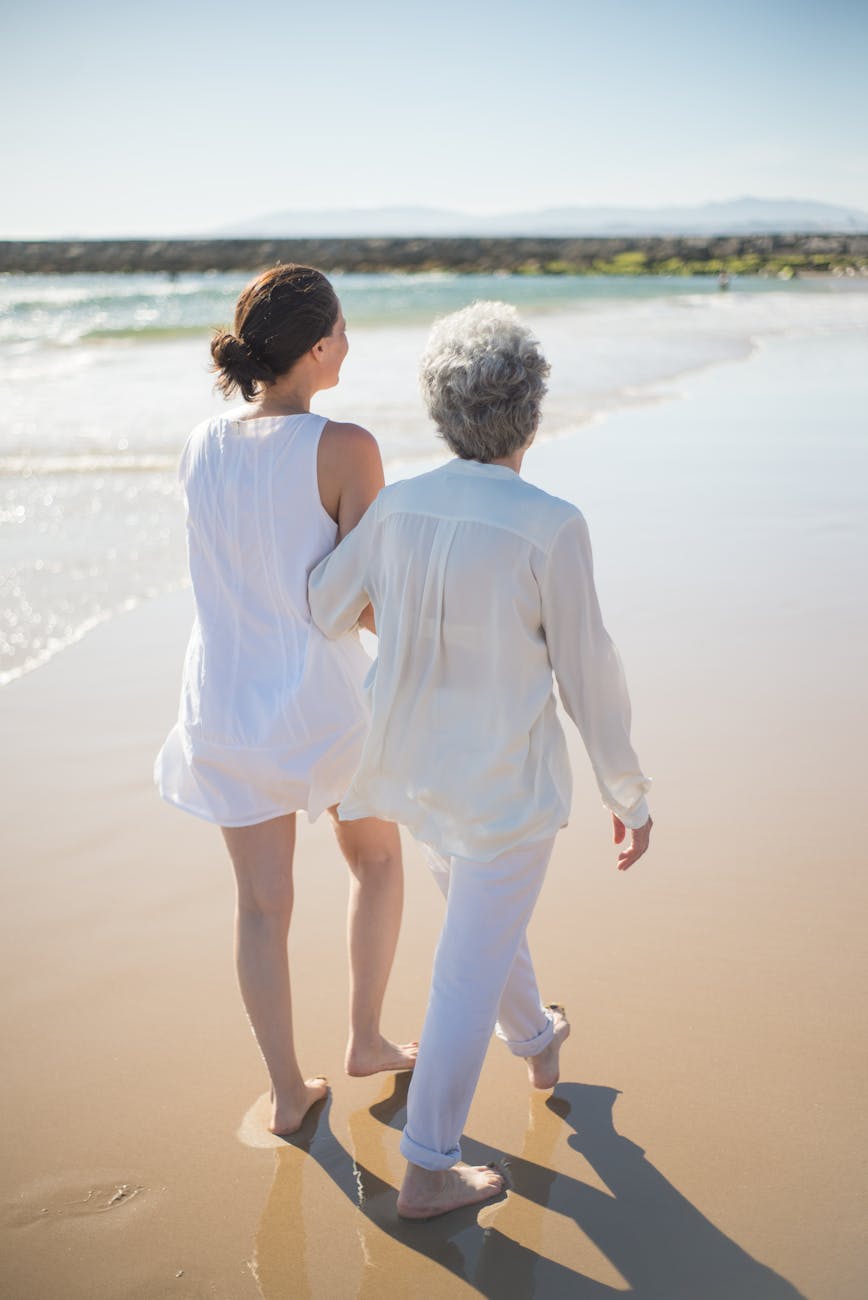 elderly woman holding on another woman while walking at the beach