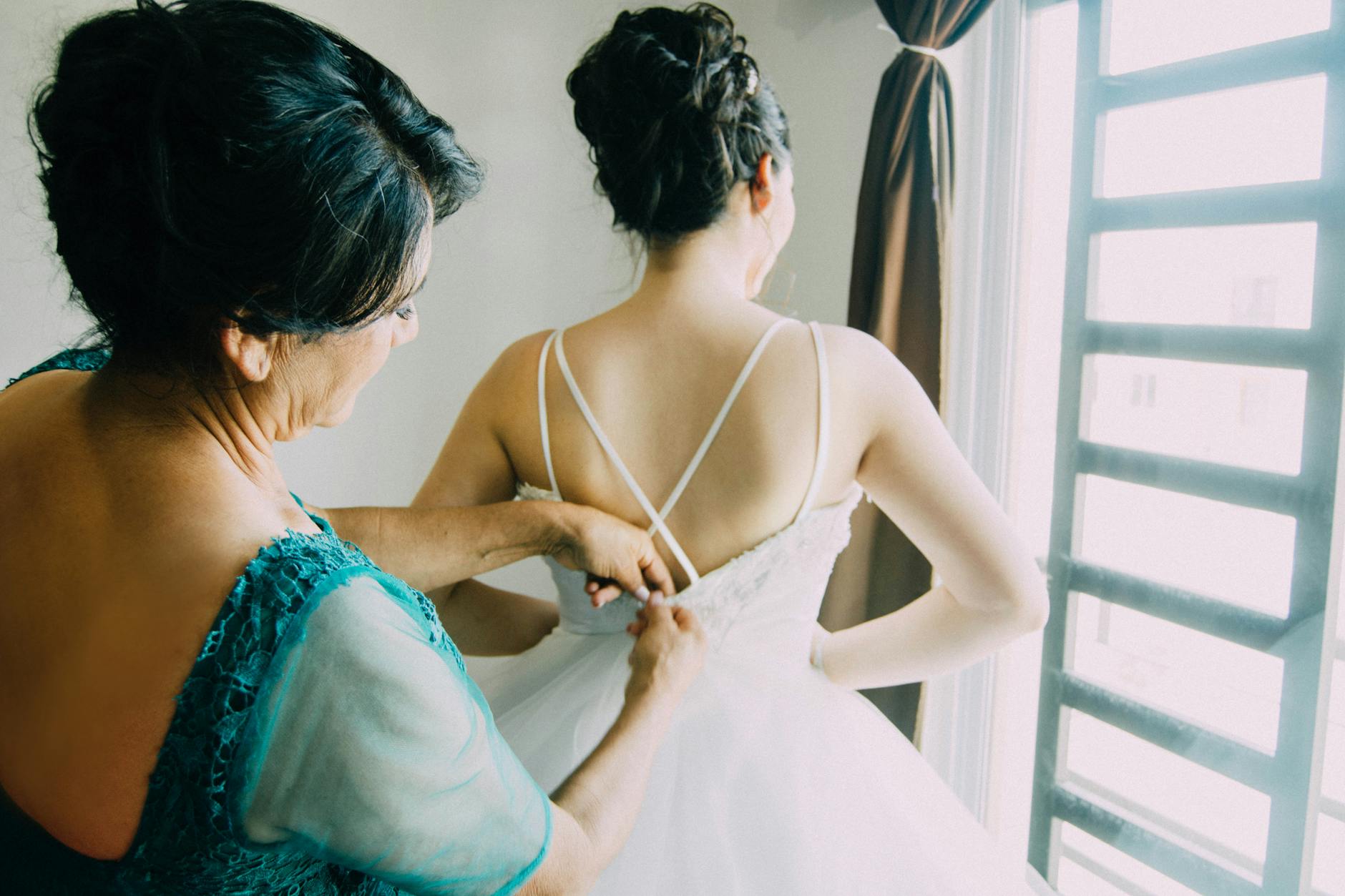 a mother zipping up the wedding dress on daughter